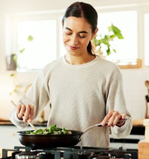 Photo shows a young woman cooking vegetables in a wok in her kitchen while reading a recipe on her phone. Around 30 million people reportedly participated in this year's "record-breaking" Veganuary 2026 campaign.