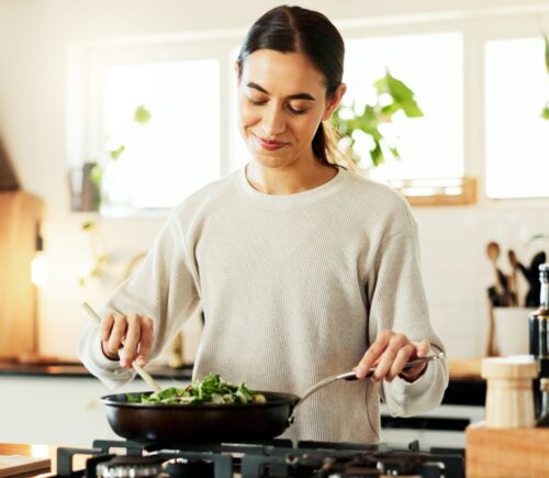 Photo shows a young woman cooking vegetables in a wok in her kitchen while reading a recipe on her phone. Around 30 million people reportedly participated in this year's "record-breaking" Veganuary 2026 campaign.