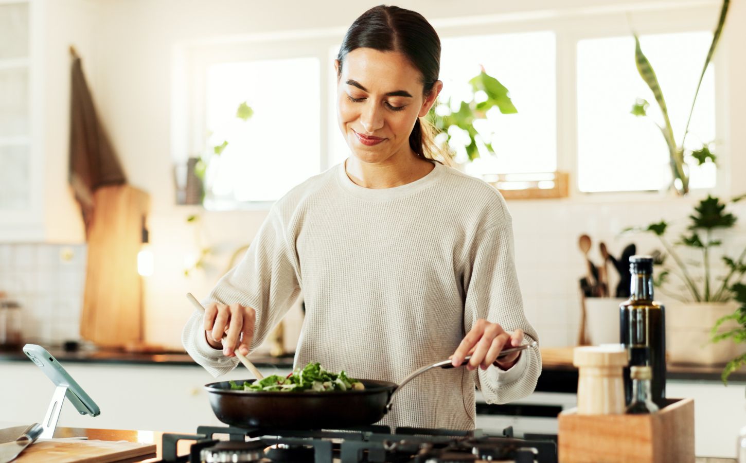 Photo shows a young woman cooking vegetables in a wok in her kitchen while reading a recipe on her phone. Around 30 million people reportedly participated in this year's "record-breaking" Veganuary 2026 campaign.