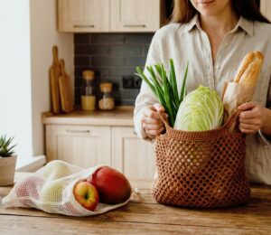 Woman unpacking groceries on her kitchen counter, with one bag full of veg and a baguette, and another of fruit, to illustrate article about how meal timing can benefit health