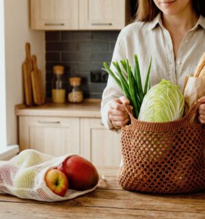 Woman unpacking groceries on her kitchen counter, with one bag full of veg and a baguette, and another of fruit, to illustrate article about how meal timing can benefit health