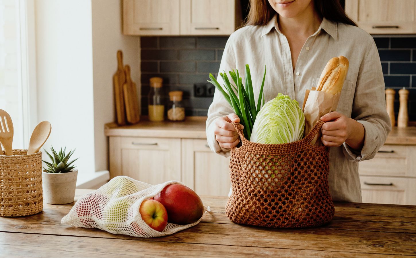 Woman unpacking groceries on her kitchen counter, with one bag full of veg and a baguette, and another of fruit, to illustrate article about how meal timing can benefit health