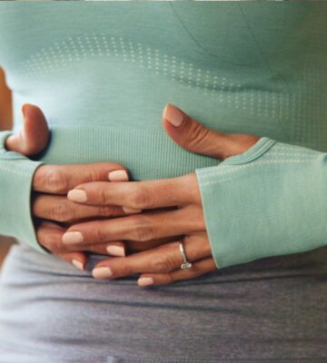 Woman holding her stomach, illustrating digestive discomfort and article exploring research on the link between vitamin B1 and IBS