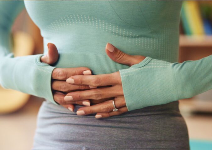 Woman holding her stomach, illustrating digestive discomfort and article exploring research on the link between vitamin B1 and IBS