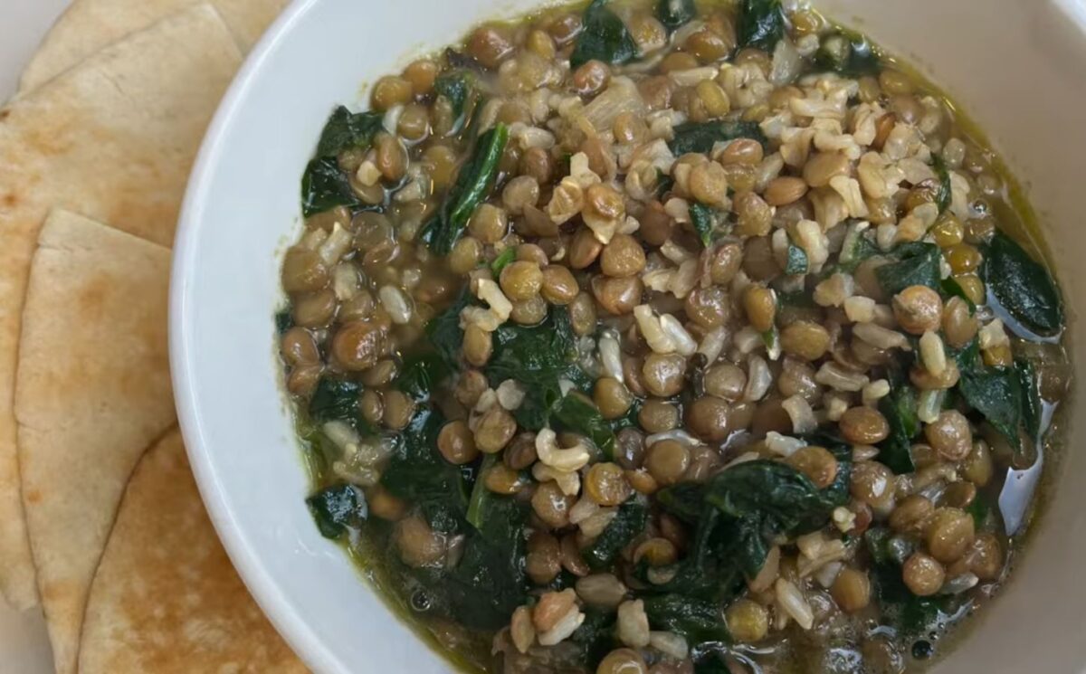 A bowl of vegan mujadara soup with added spinach and served with pita bread