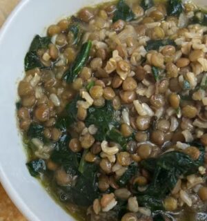 A bowl of vegan mujadara soup with added spinach and served with pita bread