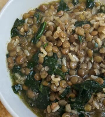 A bowl of vegan mujadara soup with added spinach and served with pita bread