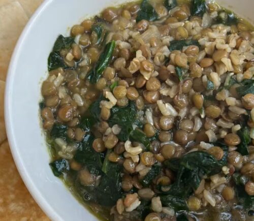 A bowl of vegan mujadara soup with added spinach and served with pita bread
