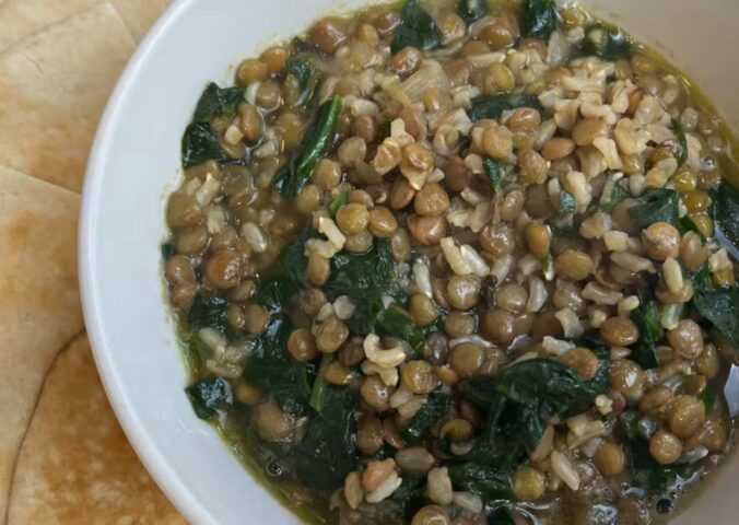 A bowl of vegan mujadara soup with added spinach and served with pita bread