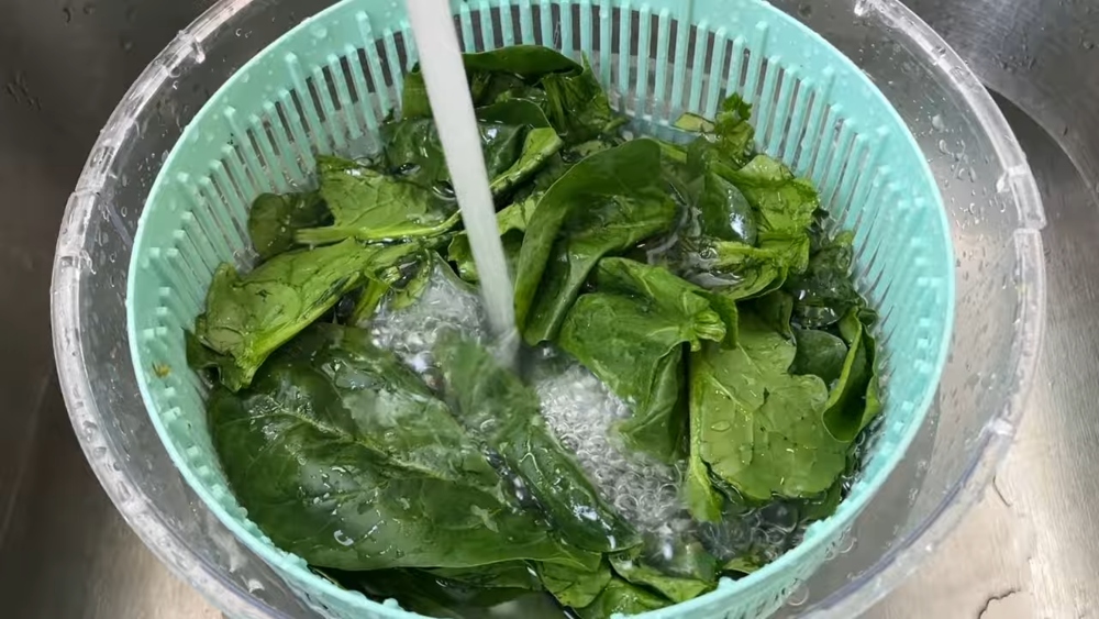 Fresh organic spinach being rinsed under running water in the sink, to be added to a vegan mujadara soup for extra iron and nutrients