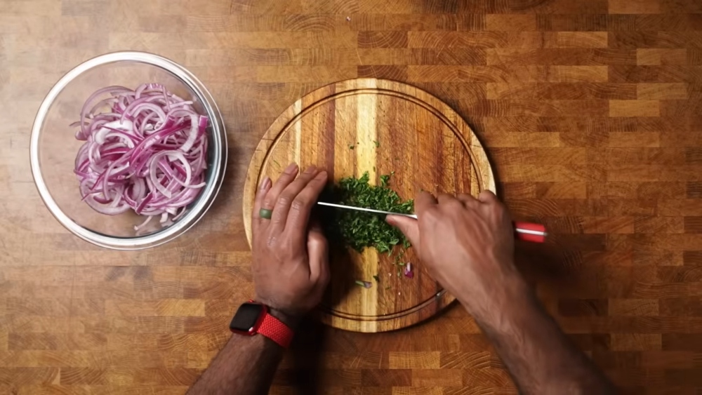 Bernard chops parsley on a cutting board to combine with sliced onions mixed with lemon juice, olive oil, salt, and sumac, a key step in this vegan shawarma recipe