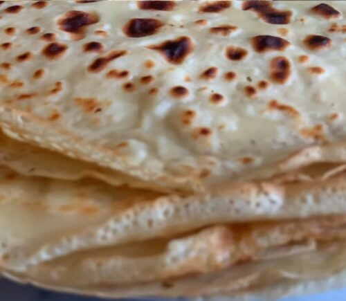 A stack of freshly cooked vegan orange zest crepes, showing their thin, golden texture