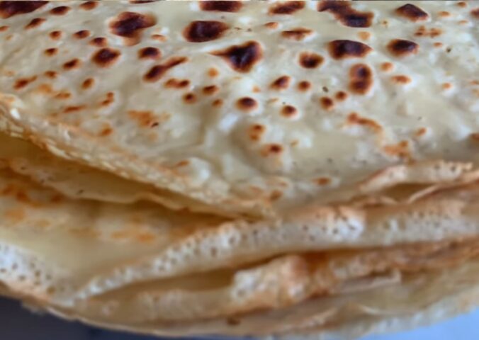 A stack of freshly cooked vegan orange zest crepes, showing their thin, golden texture