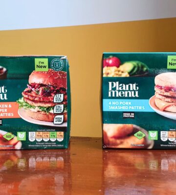 Photo shows the two "smashed" burger products from Aldi - the No Pork Smashed Patties and the No Chicken & Black Pepper Smashed Patties - on a wooden dining table against a yellow and white background