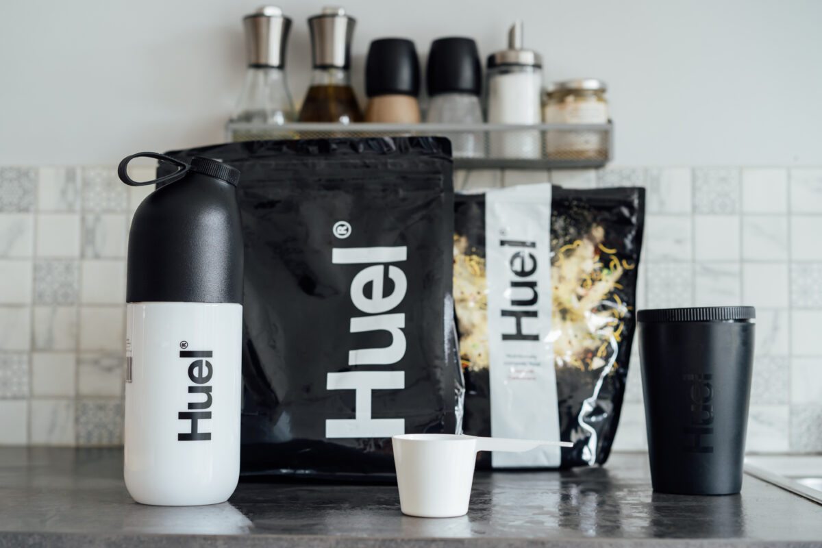 Photo shows a selection of Huel-branded products on a kitchen counter, including a shaker, protein powder, and a measuring scoop. Danone SA has agreed to buy Huel, a leading plant-based protein brand based in the UK, for €1 billion