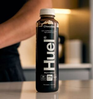 Photo shows someone's arm as they stand behind a bottle of Huel on a kitchen worktop. Danone SA has agreed to buy Huel, a leading plant-based protein brand based in the UK, for €1 billion