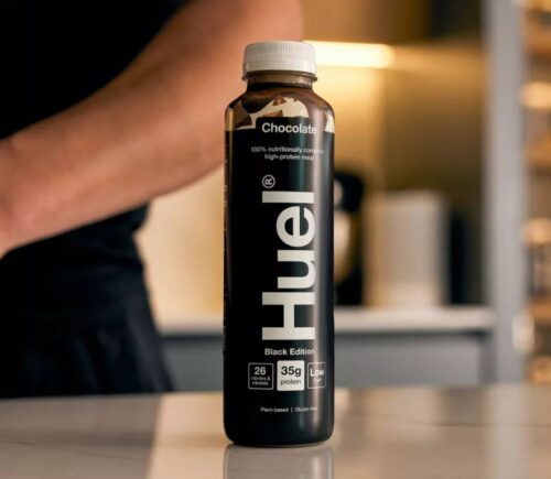 Photo shows someone's arm as they stand behind a bottle of Huel on a kitchen worktop. Danone SA has agreed to buy Huel, a leading plant-based protein brand based in the UK, for €1 billion