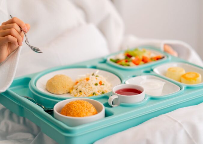 Photo shows someone eating a healthy, plant-based hospital meal in bed. A catering company has reduced hospital food emissions by 22 percent over the last year with “Greener By Default” plant-based meals