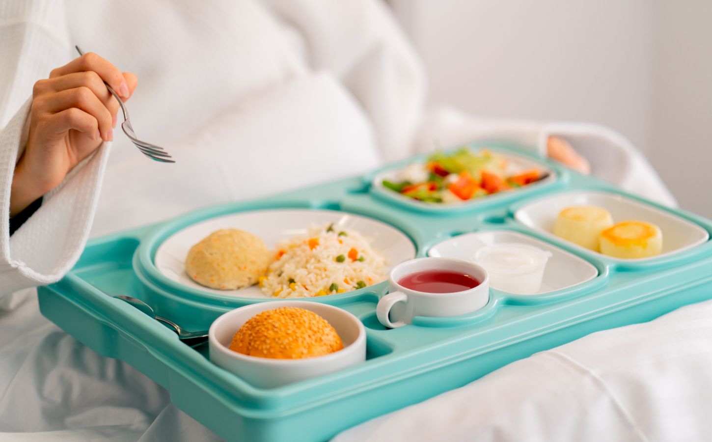Photo shows someone eating a healthy, plant-based hospital meal in bed. A catering company has reduced hospital food emissions by 22 percent over the last year with “Greener By Default” plant-based meals