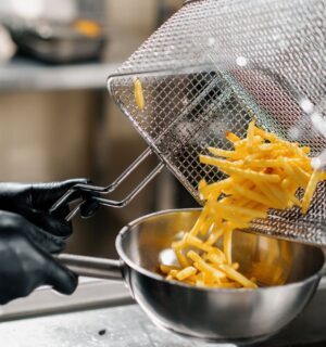 Photo shows a chef tipping fresh french fries out of a wire rack and into a metal bowl. Scientists may have figured out how to make french fries healthier by combining traditional deep frying with microwave technology