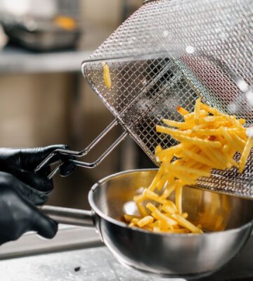 Photo shows a chef tipping fresh french fries out of a wire rack and into a metal bowl. Scientists may have figured out how to make french fries healthier by combining traditional deep frying with microwave technology