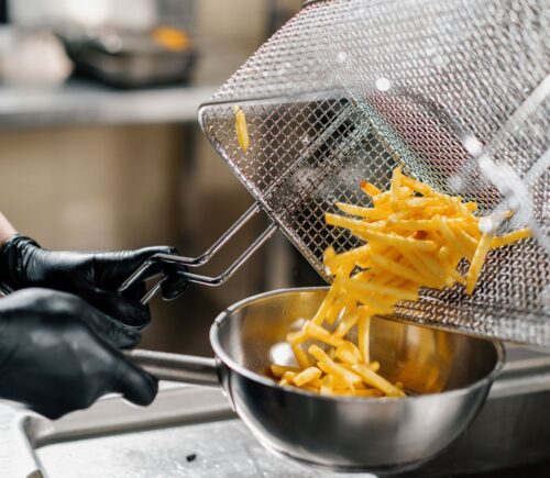 Photo shows a chef tipping fresh french fries out of a wire rack and into a metal bowl. Scientists may have figured out how to make french fries healthier by combining traditional deep frying with microwave technology