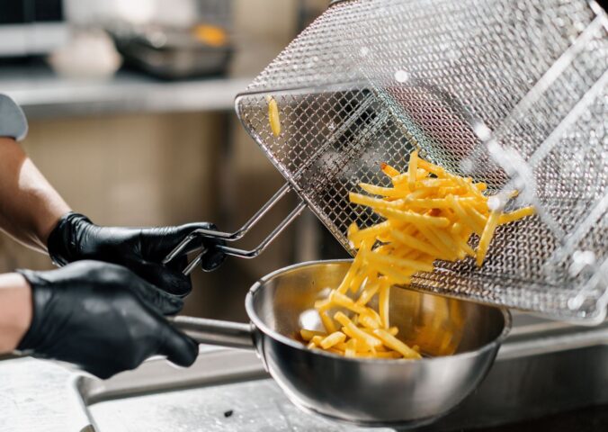 Photo shows a chef tipping fresh french fries out of a wire rack and into a metal bowl. Scientists may have figured out how to make french fries healthier by combining traditional deep frying with microwave technology