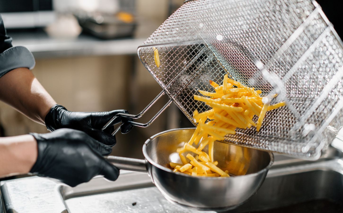 Photo shows a chef tipping fresh french fries out of a wire rack and into a metal bowl. Scientists may have figured out how to make french fries healthier by combining traditional deep frying with microwave technology