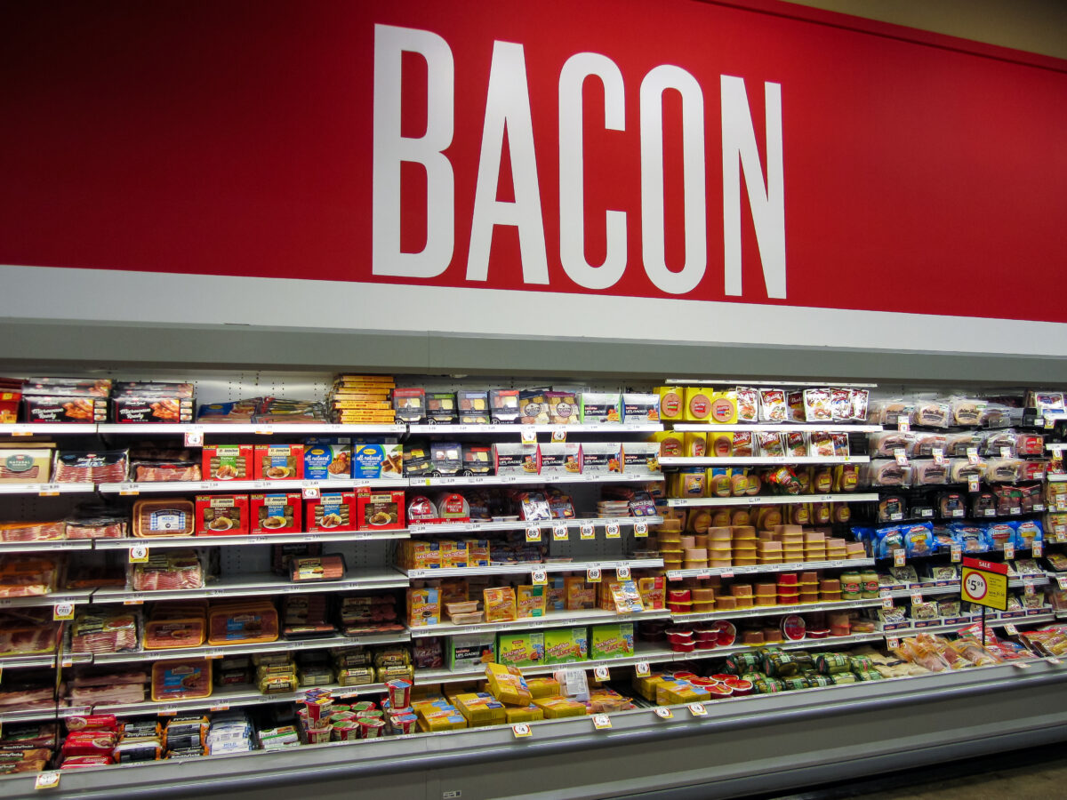 Photo shows the meat aisle in a supermarket and a large red sign that says "bacon." Sales of nitrite-cured bacon have dropped significantly as consumers look to avoid the controversial additive over its links to cancer risk.