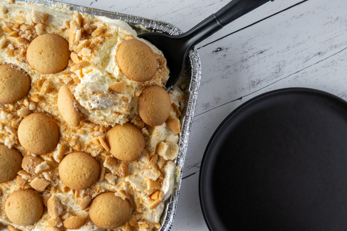 Photo shows a large tray of banana pudding on a white tablecloth. While traditional banana pudding is not vegan, it is possible to make it with a plant-based recipe