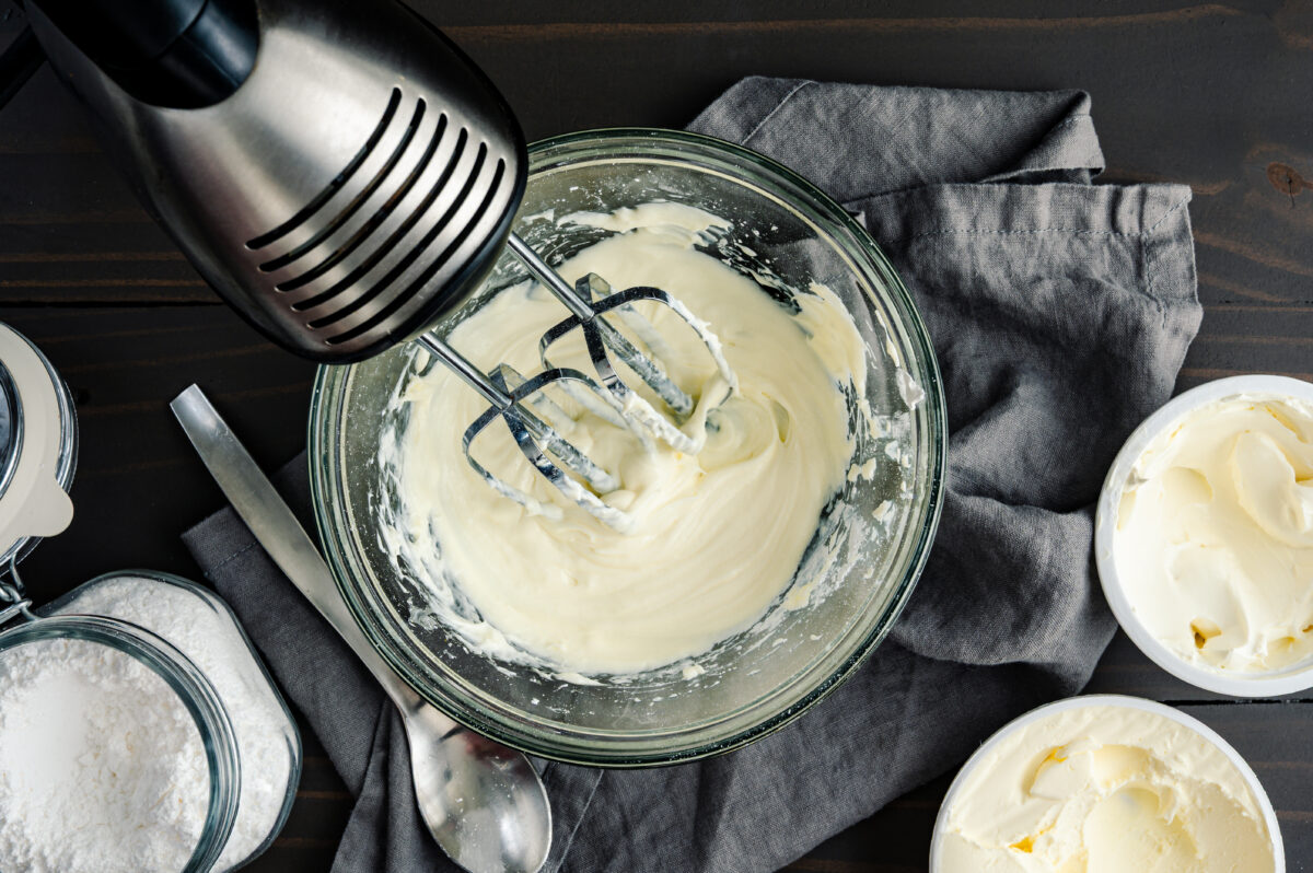 Photo shows cream being whipped with an electric whisk in a glass bowl