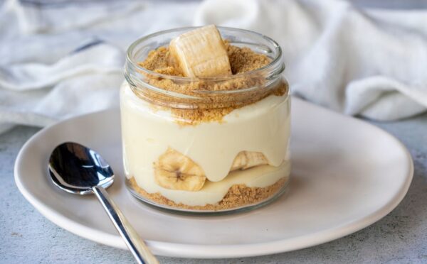 Photo shows a single serve banana pudding in a glass jar. Banana pudding is not traditionally vegan-friendly, but it can be easily made vegan with the use of common plant-based ingredients like coconut cream and oat milk