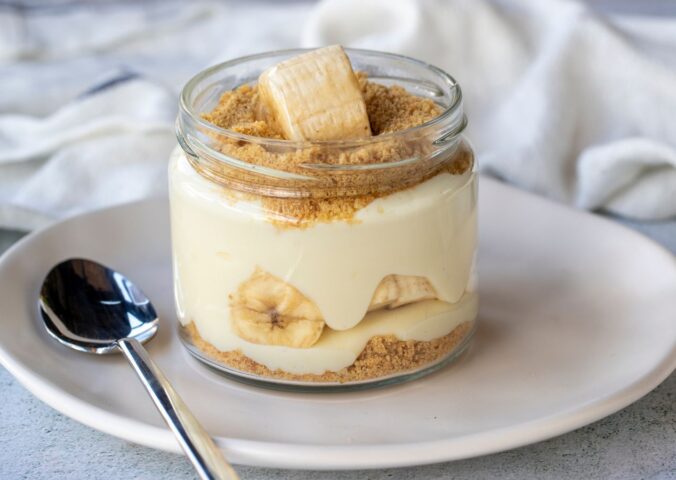 Photo shows a single serve banana pudding in a glass jar. Banana pudding is not traditionally vegan-friendly, but it can be easily made vegan with the use of common plant-based ingredients like coconut cream and oat milk