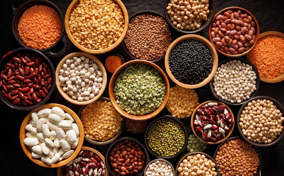 Bowls of different legumes including beans, lentils, and peas arranged on a black background, viewed from above, an example of foods that help heal your gut