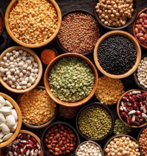 Bowls of different legumes including beans, lentils, and peas arranged on a black background, viewed from above, an example of foods that help heal your gut