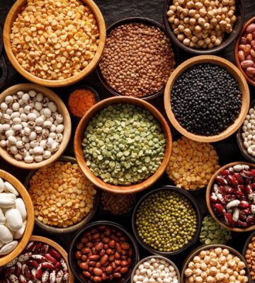 Bowls of different legumes including beans, lentils, and peas arranged on a black background, viewed from above, an example of foods that help heal your gut