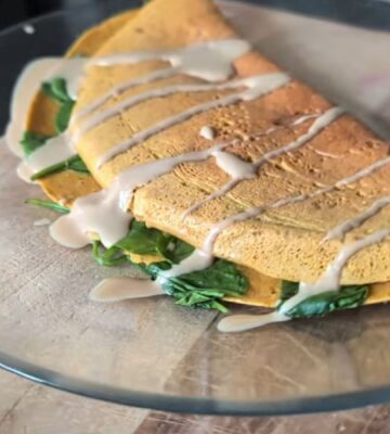 Chickpea omelette drizzled with tahini on a plate, one of Daynesh's quick vegan breakfasts.