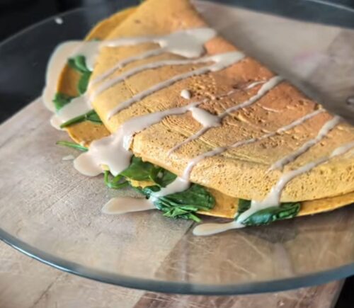 Chickpea omelette drizzled with tahini on a plate, one of Daynesh's quick vegan breakfasts.