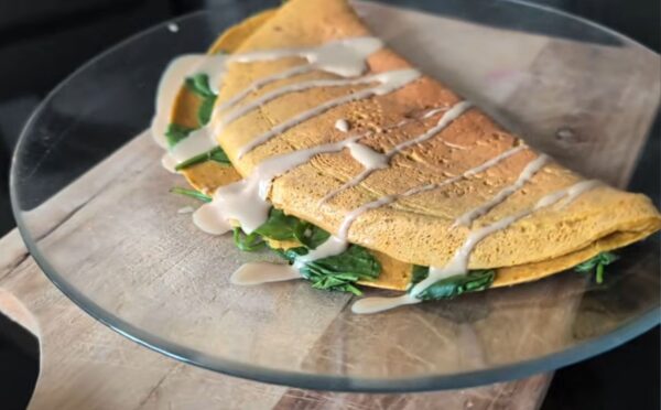 Chickpea omelette drizzled with tahini on a plate, one of Daynesh's quick vegan breakfasts.