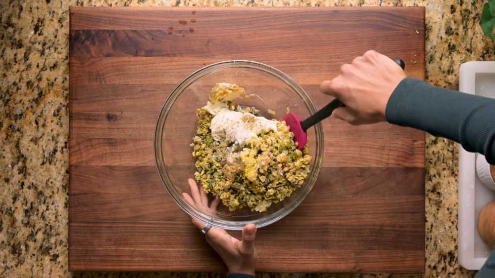 Vora mixes the chickpea salad is in a glass bowl on a wooden cutting board. This is one of her 3 vegan chickpea recipes.