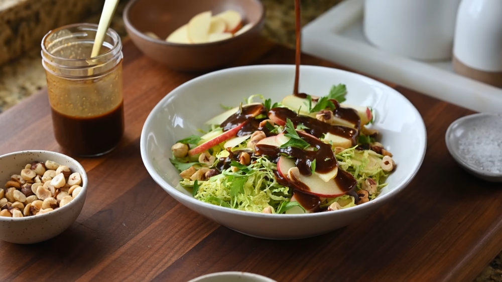 Photo of a shaved Brussels sprout salad drizzled with a creamy homemade salad dressing and topped with apple slices and hazelnuts