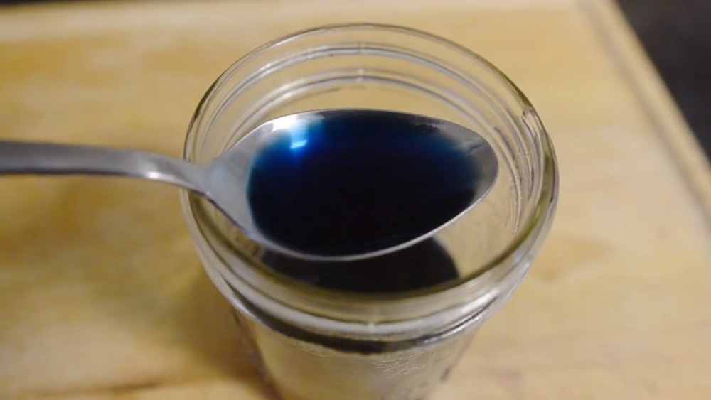 Couse holds the finished blue dye in a spoon, created for the ocean layer of her Earth Day vegan cheesecake