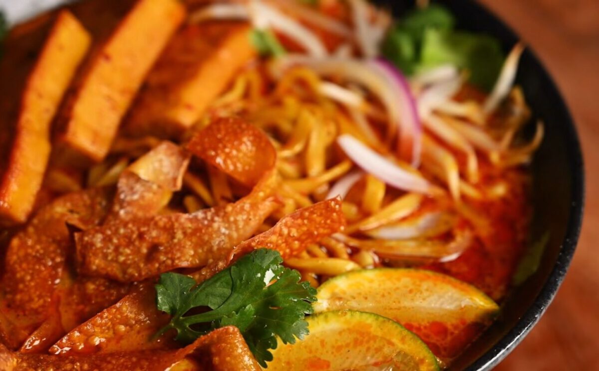 Bowl of vegan khao soi containing seared tofu, baked dumpling wrapper strips, cilantro, and lemon, in a coconut-curry broth