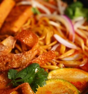 Bowl of vegan khao soi containing seared tofu, baked dumpling wrapper strips, cilantro, and lemon, in a coconut-curry broth