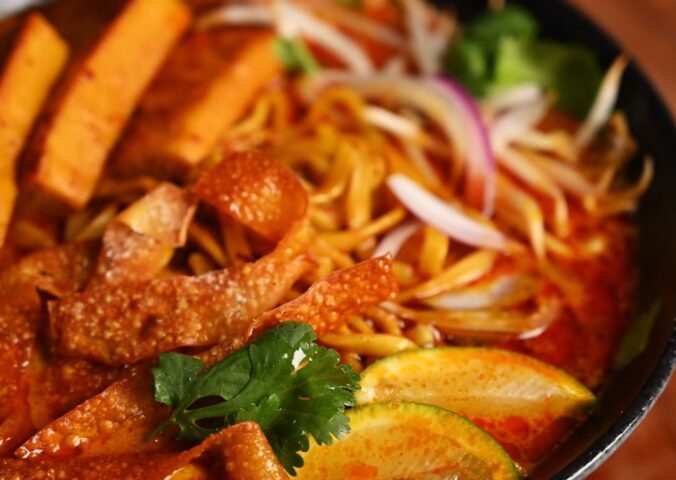 Bowl of vegan khao soi containing seared tofu, baked dumpling wrapper strips, cilantro, and lemon, in a coconut-curry broth