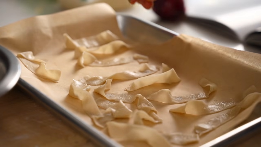 Thin dumpling wrapper strips spread on a baking tray over parchment paper. Once baked, they'll add a crispy texture to the vegan khao soi. 