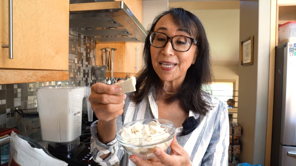 Schinner in her kitchen, holding a bowl of deodorized cocoa butter and lifting a piece to show its texture, an essential ingredient in her vegan parmesan recipe