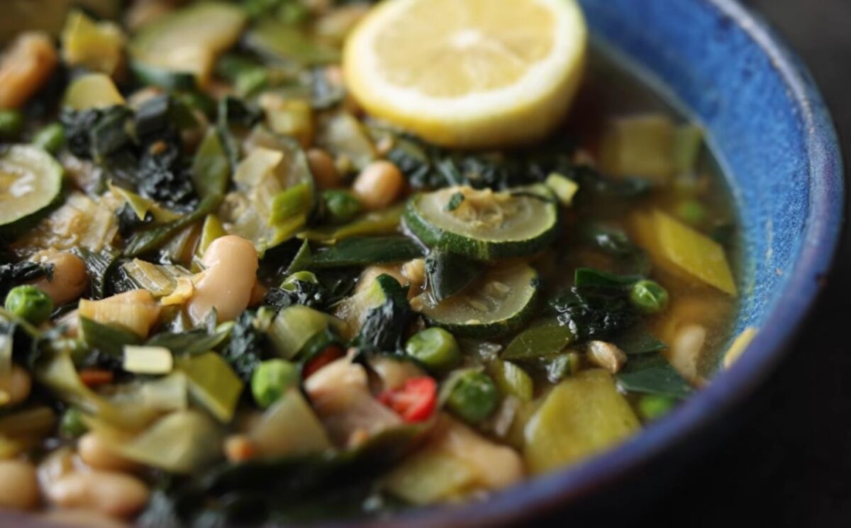 Vegan longevity stew with cannellini beans and leafy greens, served in a blue bowl and topped with a decorative lemon slice