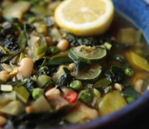 Vegan longevity stew with cannellini beans and leafy greens, served in a blue bowl and topped with a decorative lemon slice