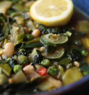 Vegan longevity stew with cannellini beans and leafy greens, served in a blue bowl and topped with a decorative lemon slice